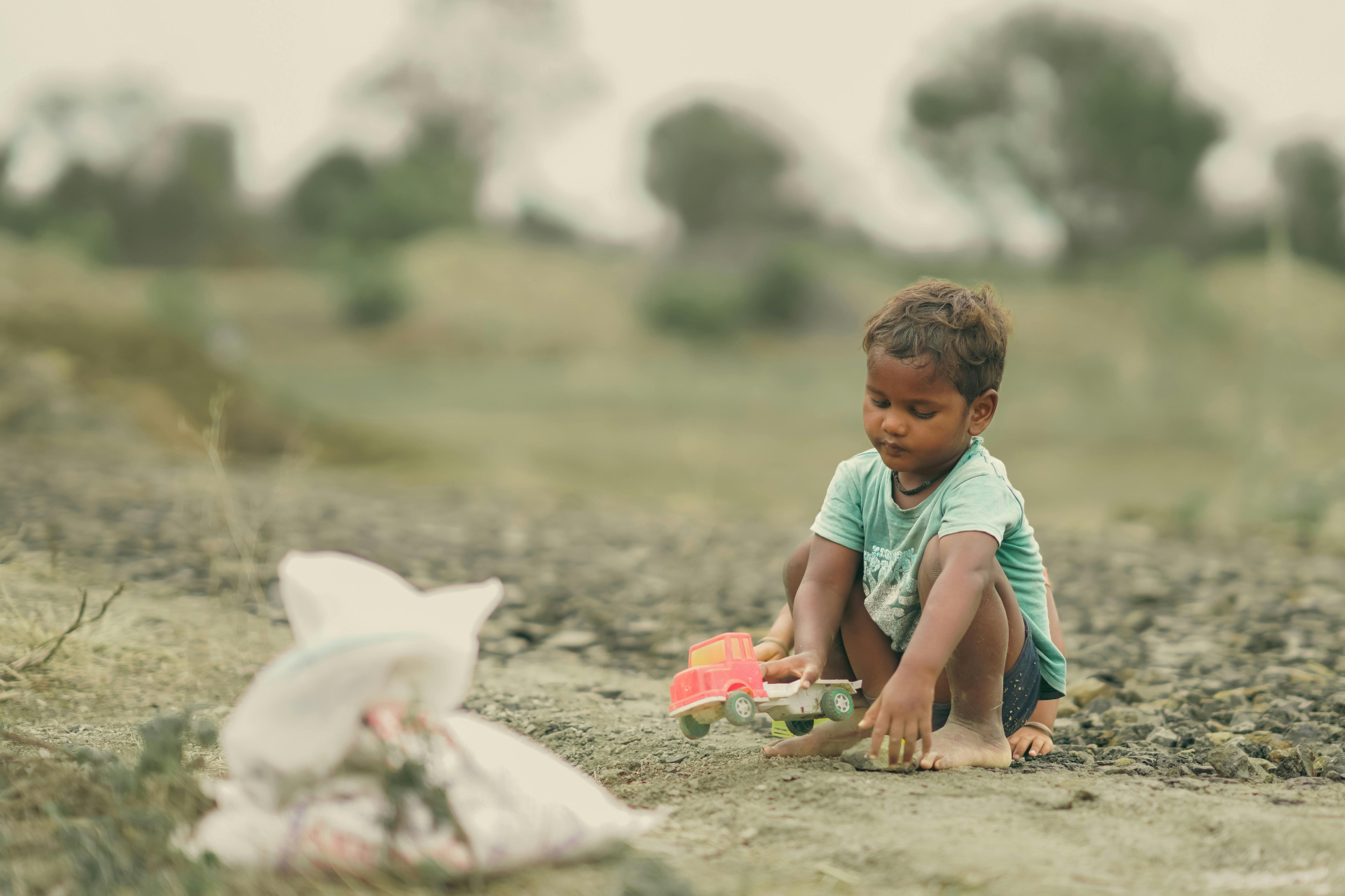 A imagem mostra uma criança brincando com um carrinho em um terreno sem asfalto