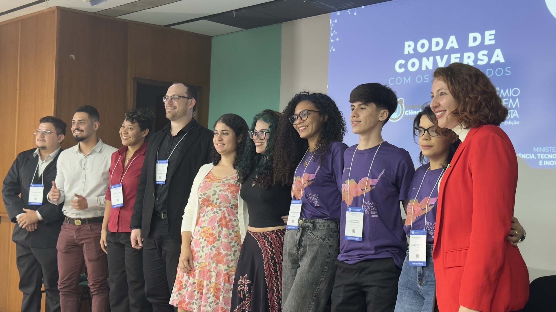 A imagem mostra um grupo de participantes e convidados reunidos para uma foto durante um evento educacional ou científico.  Ao fundo, uma tela de projeção exibe o título “Roda de Conversa com os Vencedores”, associado ao Prêmio Jovem Cientista, indicando que a atividade faz parte da programação do evento.