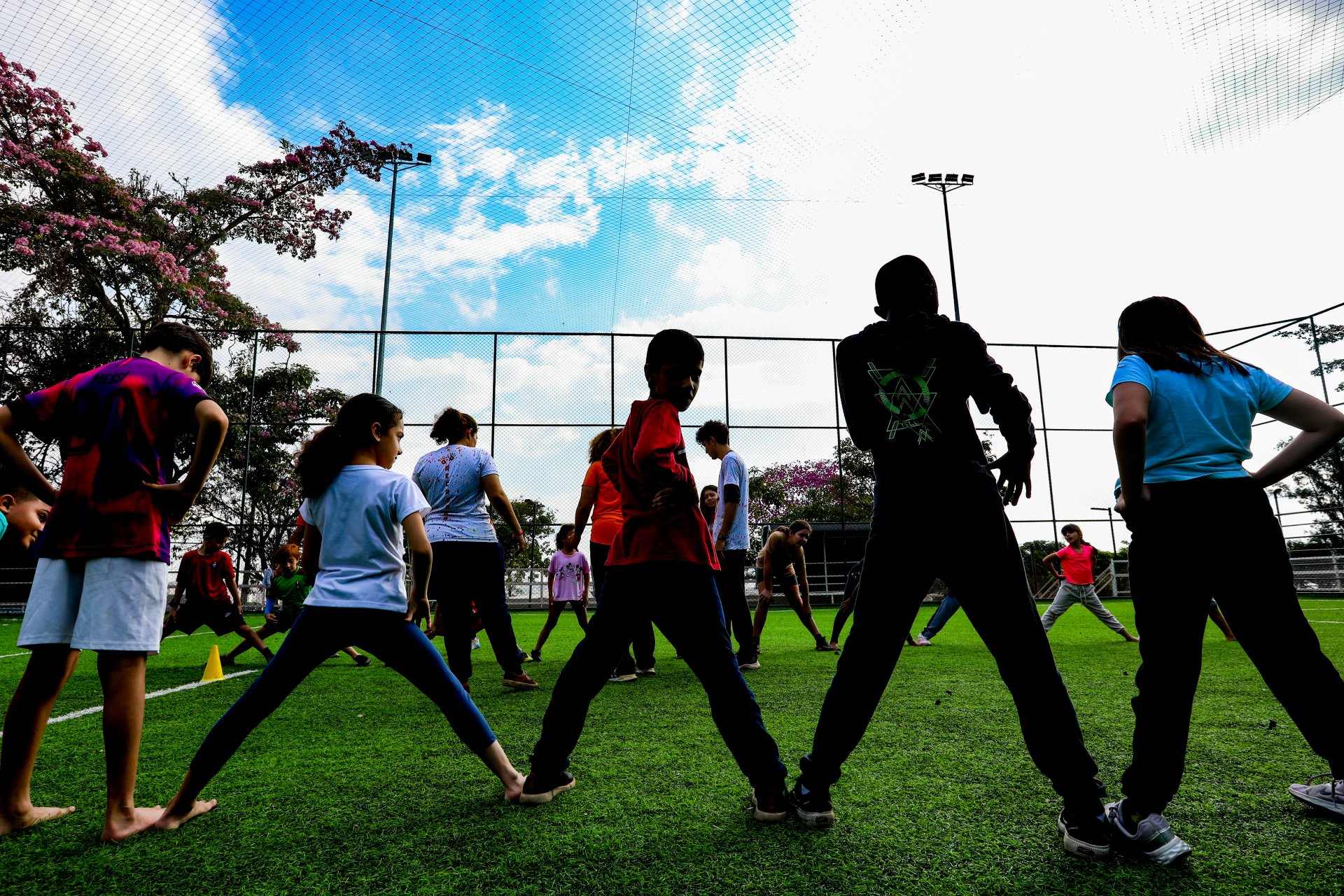 A imagem mostra um grupo de crianças organizadas em uma roda em um campo de futebol