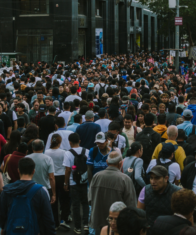 A imagem mostra uma rua com diversas pessoas atravessando nos dois sentidos