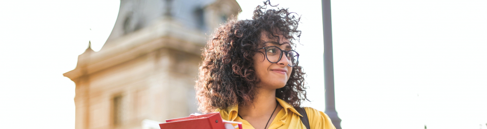 Mulher com cabelo enrolado olha para a direita, com uma igreja ao fundo.