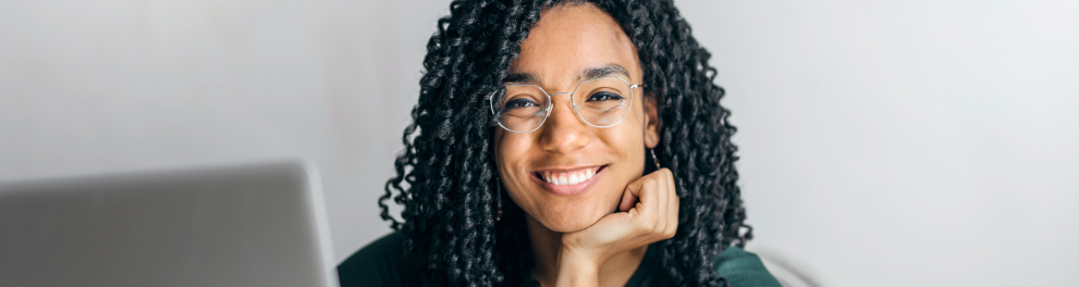 jovem sorrindo sentada a frente de uma mesa com laptop