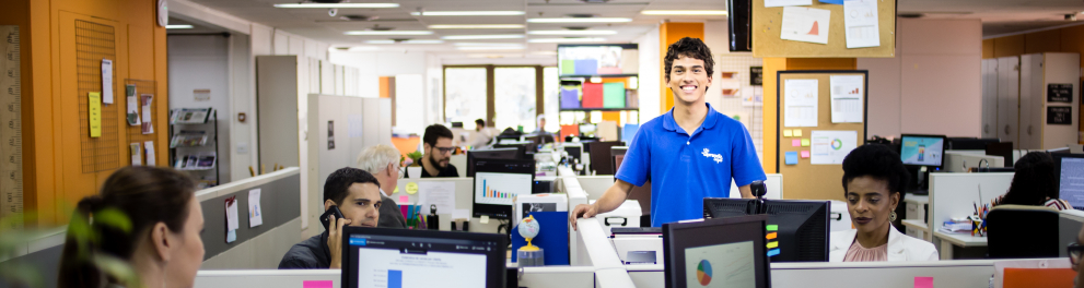 Jovem aprendiz na empresa entre baias de trabalho com computadores