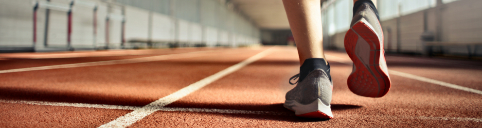Imagem com uma pista de atletismo, mostrando as pernas de um atleta em vias de dar o promeiro passo.