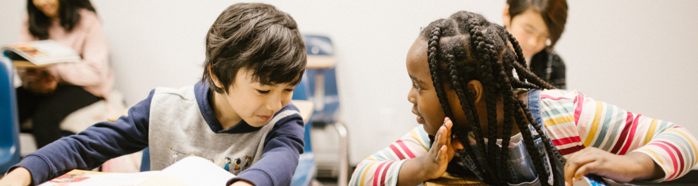 Duas crianças, um menino e uma menina, conversam na sala de aula.
