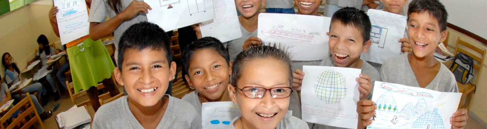 Crianças sorriem ao mostrar papeis com trabalhos escolares feitos por elas e eles.