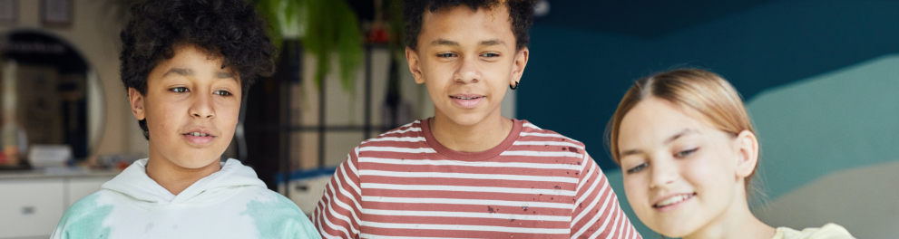 Dois meninos e uma menina observam, com curiosidade, algo que não aparece na imagem.