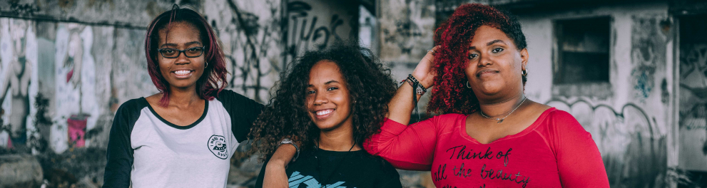 três jovens com um cenário de paredes pixadas ao fundo