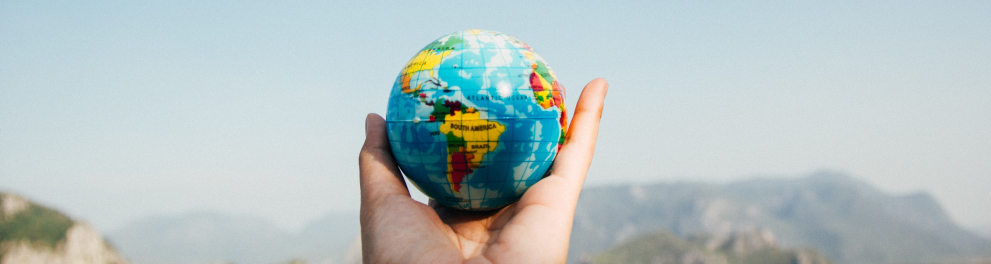 mão segurando um globo terrestre com uma paisagem natural ao fundo