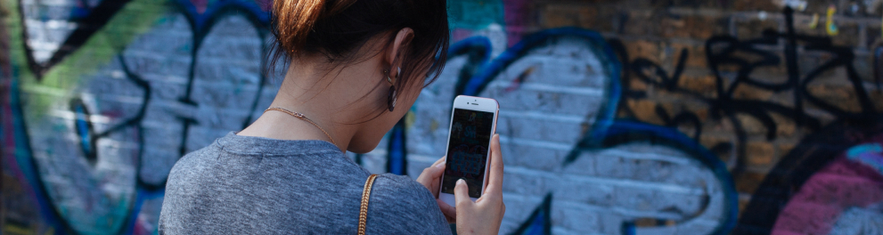 Menina filma com seu celular muro com grafite.