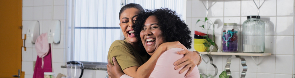 Duas mulheres se abraçam sorrindo.