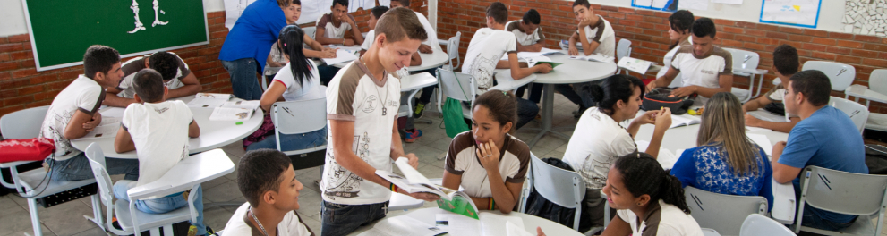 Vários e várias estudantes organizados em mesas redondas.