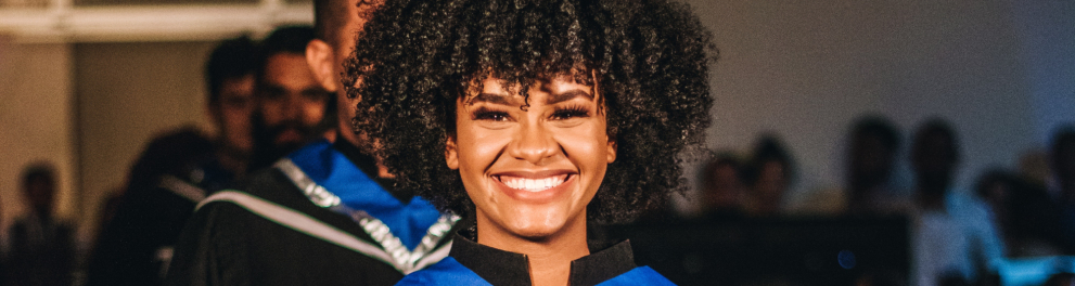 Mulher negra sorri enquanto recebe seu diploma.