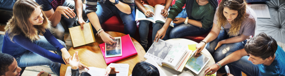 Várias e vários jovens estão sentados ao redor de uma mesa com alguns livros.