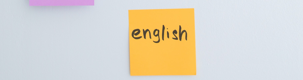 Um papel quadrado, amarelo, está sobre uma superfície branca. No papel, em letras pretas, a palavra "english".