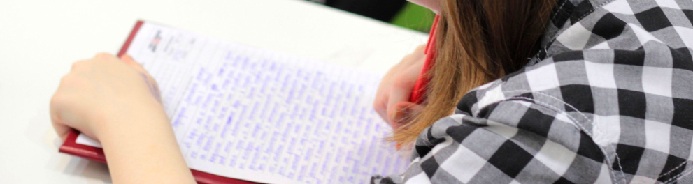 Uma menina branca escreve com uma caneta vermelha em um caderno.