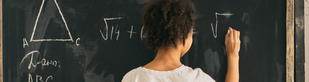Menina negra está escrevendo uma questão matemática no quadro da sala de aula.