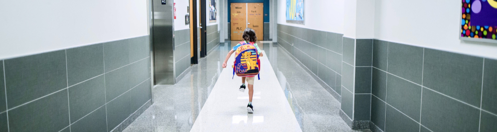 Uma criança está com sua mochila no corredor da escola.