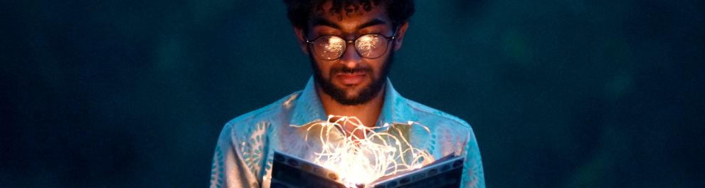 Um homem negro, usando óculos, segura um livro em que há fios iluminados.