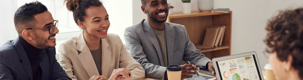 pessoas em um ambiente de trabalho sentadas em uma mesa de reunião com papéis e um laptop 