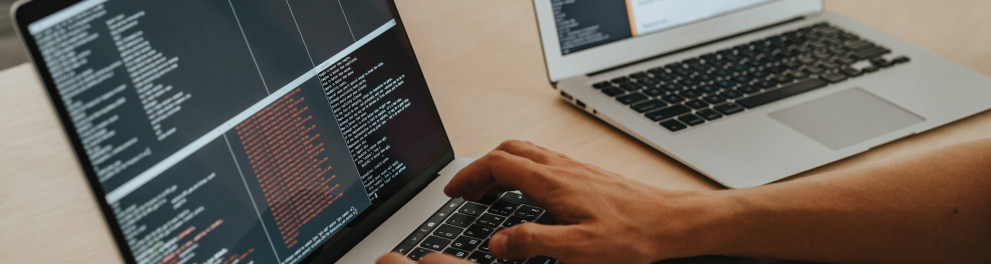 destaque nas mãos de um homem digitando em uma laptop sobre uma mesa de madeira algum tipo de código de programação