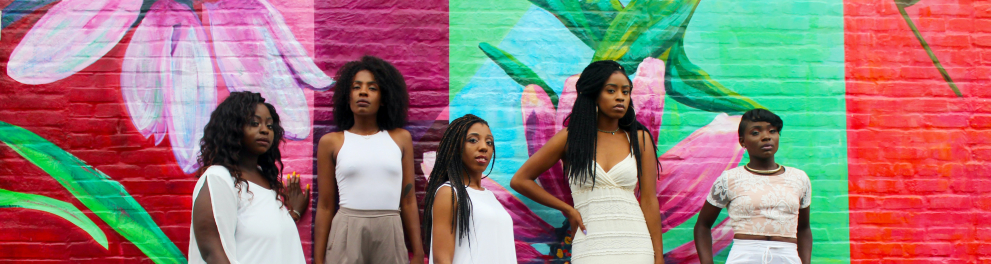 Um grupo de mulheres negras posando para uma foto em frente a um muro com flores pintadas