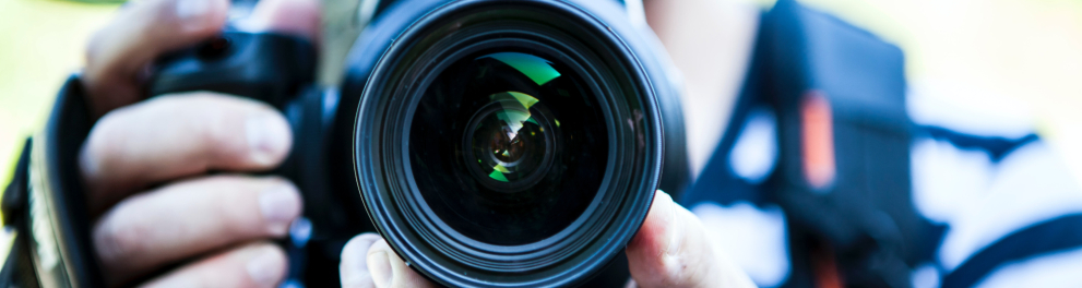 Um homem branco segura uma câmera de frente para quem o fotografou.