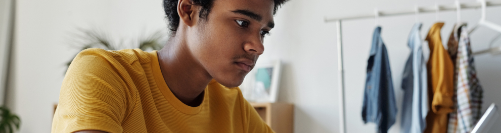 Um jovem está sentado enquanto mexe em um tablet.