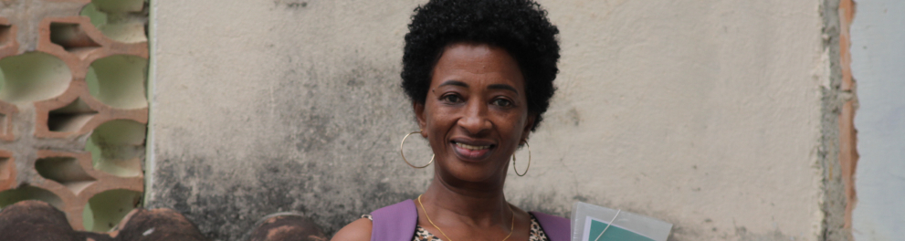 Uma mulher negra com mochila nas costas, segurando uma pasta e sorrindo para a foto