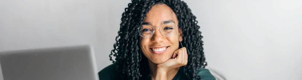 Uma jovem negra sentada em frente a um notebook e sorrindo para a foto