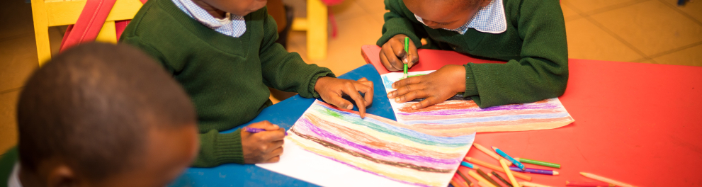 Três crianças colorindo um papel em uma sala de aula
