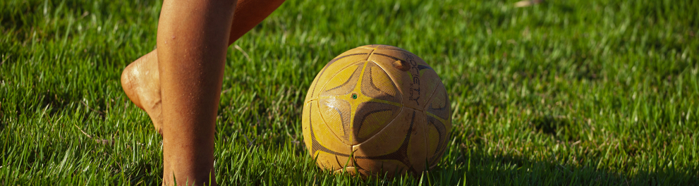 Uma bola de futebol em um gramado e um rapaz descalço ao lado