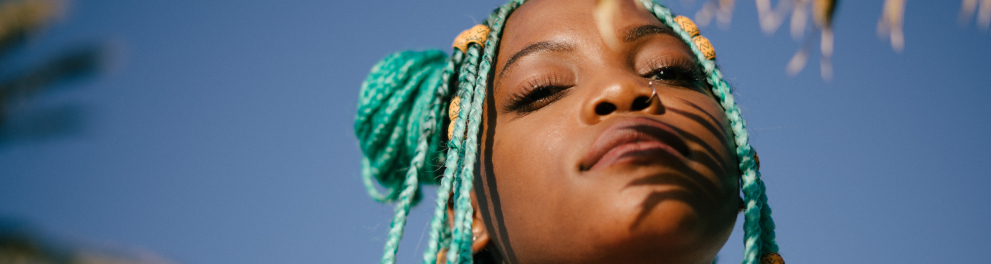 A imagem mostra uma jovem negra com tranças verdes