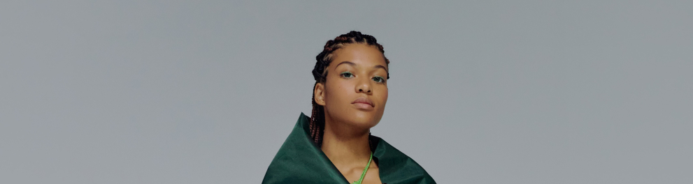 Uma mulher negra usando uma capa verde e posando para a foto