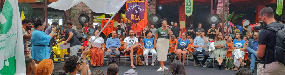 Diversas pessoas reunidas, de pé, em torno de nove outras que estão sentadas ao centro.