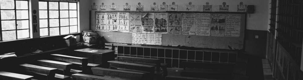Uma sala de aula vazia mostrando apenas as cadeiras, o quadro negro ao fundo e a luz apagada, sendo iluminada apenas com a luz solar que vem das janelas de vidro