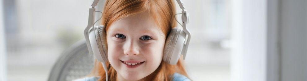 Uma jovem menina sorrindo usando headfone e sentada com os braços sobre uma mesa