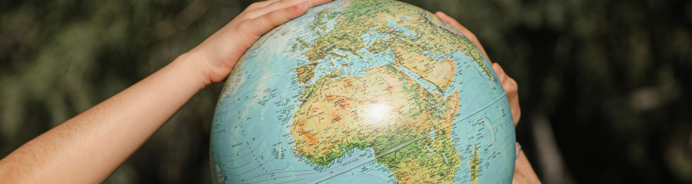 Um globo terrestre em miniatura sendo segurado por quatro mãos de duas pessoas 