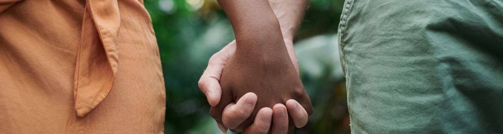 Uma mão masculina branca com os dedos entrelaçados com dedos de uma mão feminina negra