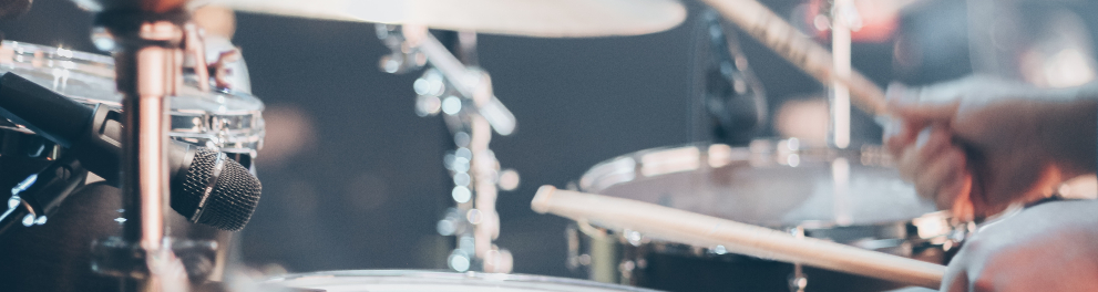 Imagem focalizada nas mãos de um baterista segurando as baquetas e tocando o instrumento