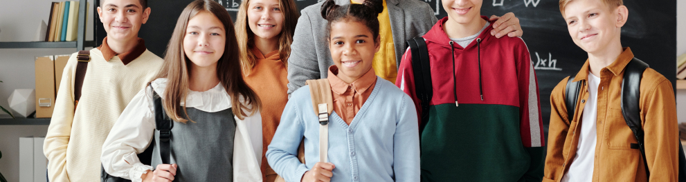 Seis alunos adolescentes posando para a foto ao lado do professor dentro de sala de aula, com o quadro negro ao fundo da imagem
