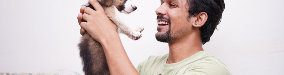 Um homem de cavanhaque está sorridente e olhando feliz para um filhote de cachorro que ele próprio está segurando com as duas mãos