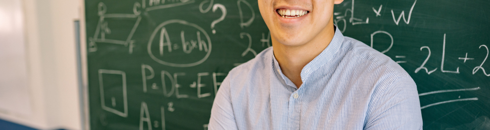 Imagem mostra um Homem de óculos sorrindo em frente a quadro negro.