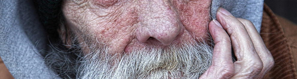 Imagem mostra um homem idoso olhando com semblante triste para o horizonte.