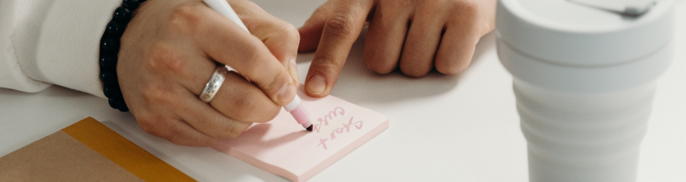Imagem mostra uma mão escrevendo em post-it.