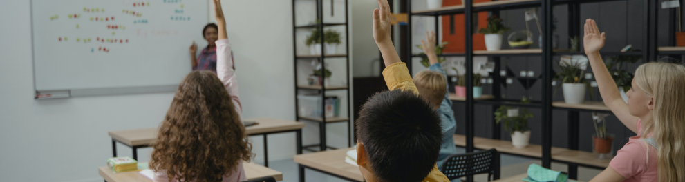 Imagem mostra alunos levantando as mãos.