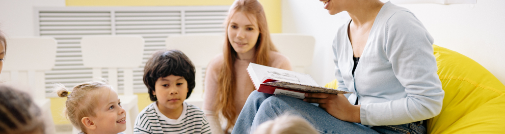 Imagem mostra professora lendo para alunos.