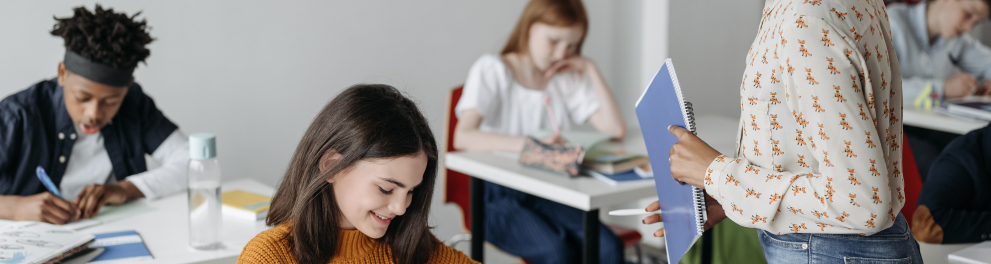 Imagem mostra uma professora interagindo com uma aluna.