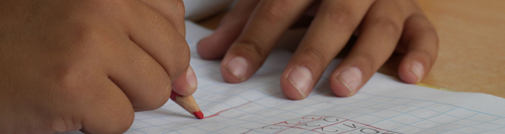 Imagem mostra uma mão segurando lápis escrevendo sobre caderno