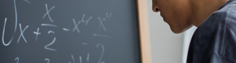 Imagem mostra uma Mulher resolvendo equação no quadro negro